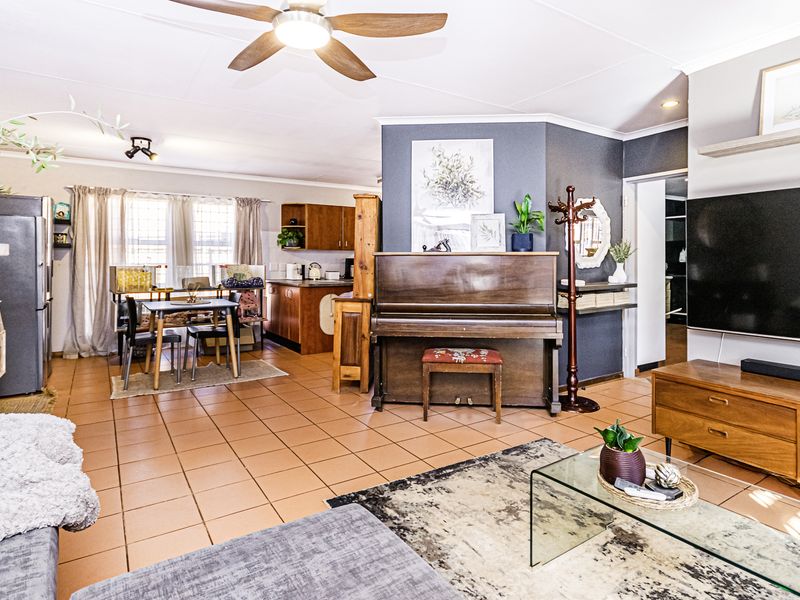 Spacious open-plan living and dining area featuring tiled flooring, a ceiling fan, and an integrated kitchen space with wooden cabinetry.