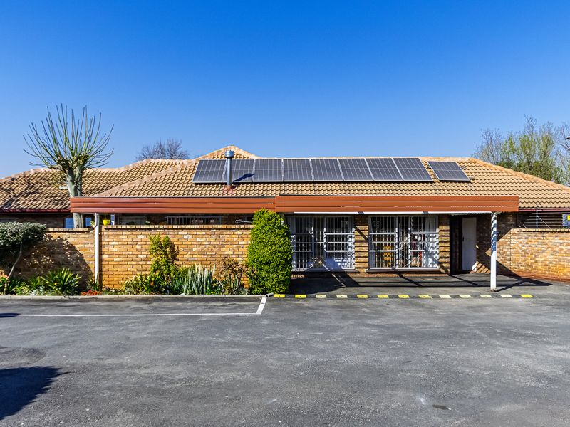 Front exterior view of a single-story brick house featuring a tiled roof, installed solar panels, and a paved driveway area.