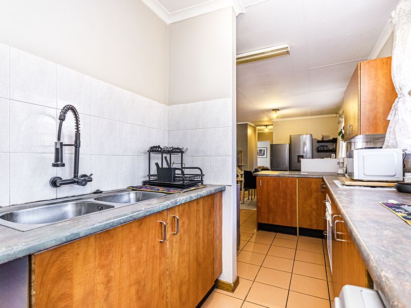 A functional kitchen featuring wooden cabinetry, laminate countertops, a double bowl sink with a modern faucet, and tiled flooring.