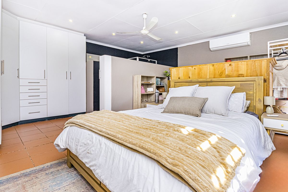 Spacious bedroom featuring built-in wardrobes, tiled flooring, a ceiling fan, and a wall-mounted split-system air conditioner for climate control.