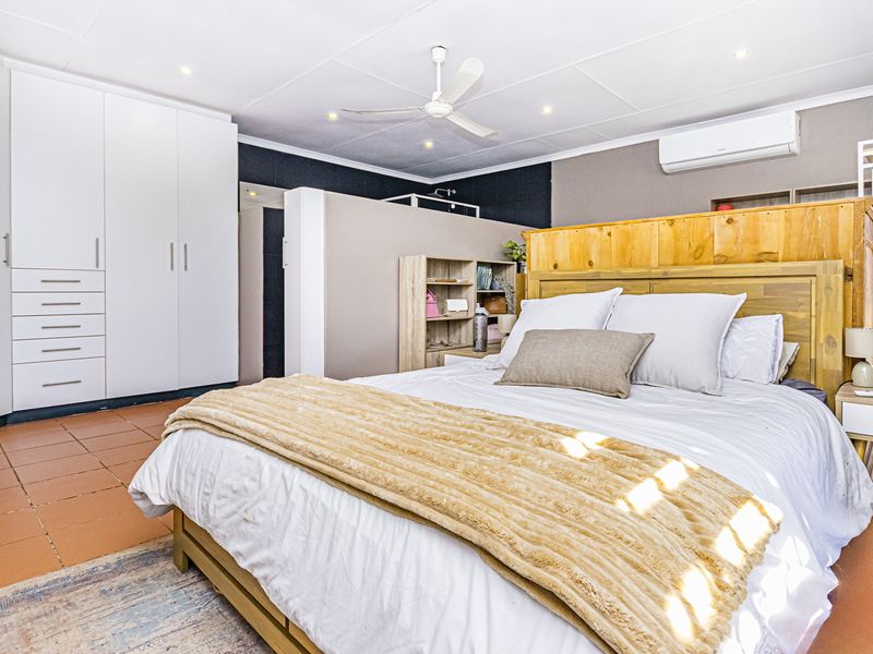 Spacious bedroom featuring built-in wardrobes, tiled flooring, a ceiling fan, and a wall-mounted split-system air conditioner for climate control.