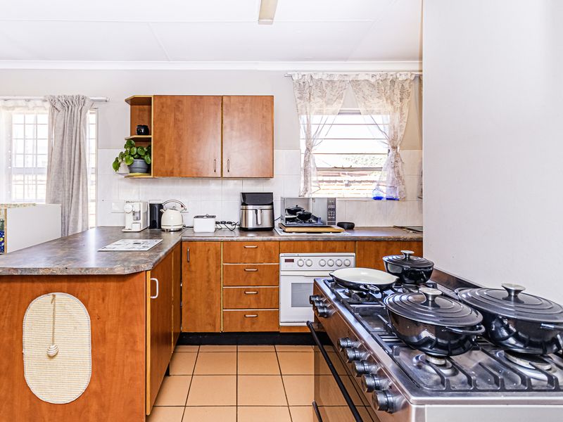 A functional kitchen featuring wood-look laminate cabinetry, tiled flooring, a gas hob, and a built-in oven, offering a practical layout for daily cooking.