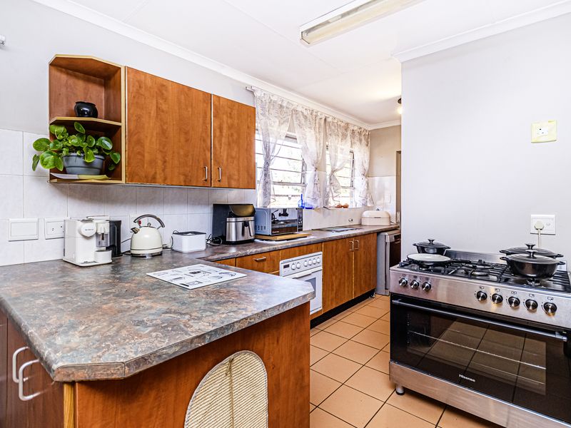 A functional kitchen featuring wooden cabinetry, laminate countertops, tiled flooring, and a freestanding gas stove with an electric oven.