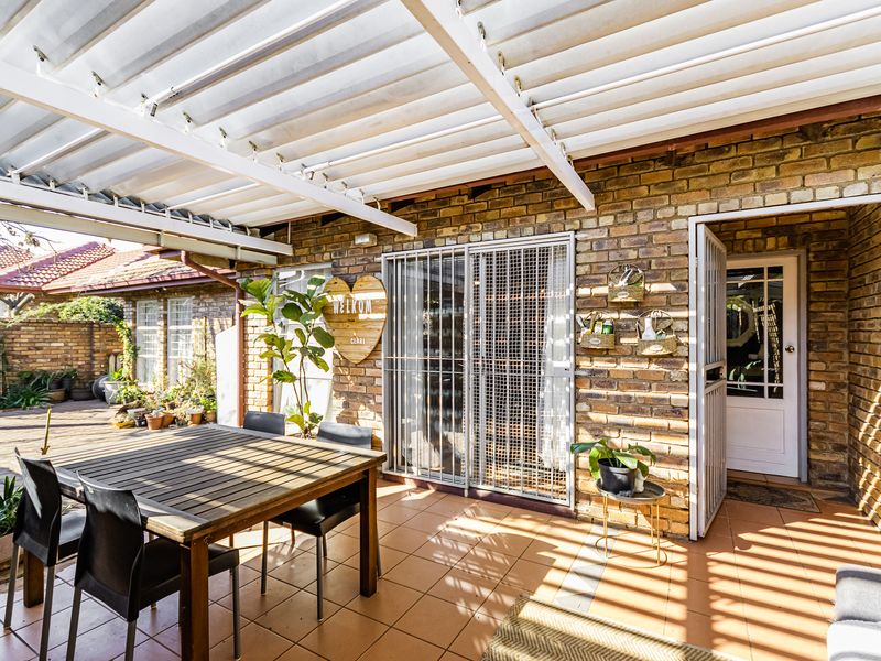 A covered outdoor patio area featuring exposed brick walls, tiled flooring, and a corrugated roof structure, providing a functional space for outdoor living.