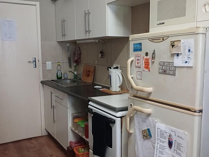 A compact kitchen featuring white cabinetry, a stainless steel sink, tiled backsplash, and a freestanding stove, providing functional storage and preparation space.
