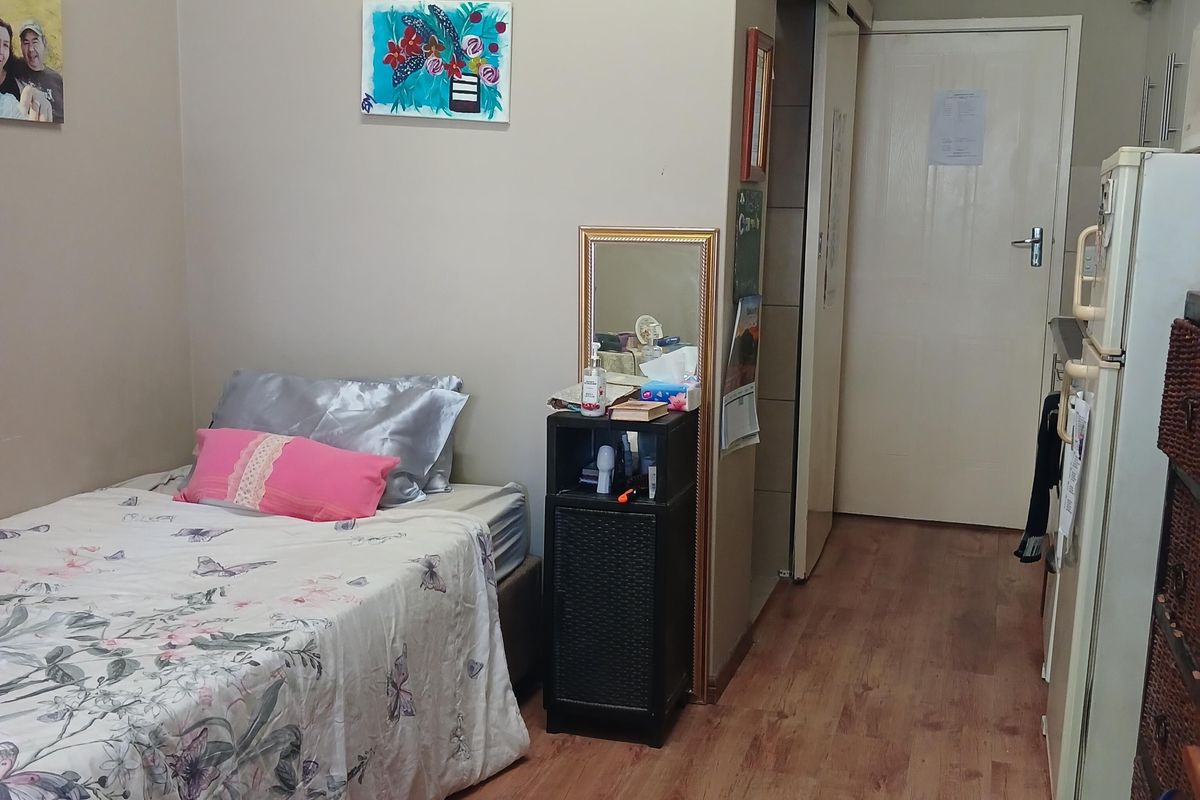 A compact bedroom featuring laminate flooring and a high-level transom window, providing a functional living space.
