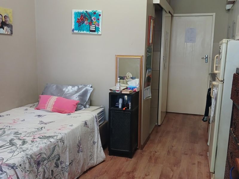 A compact bedroom featuring laminate flooring and a high-level transom window, providing a functional living space.