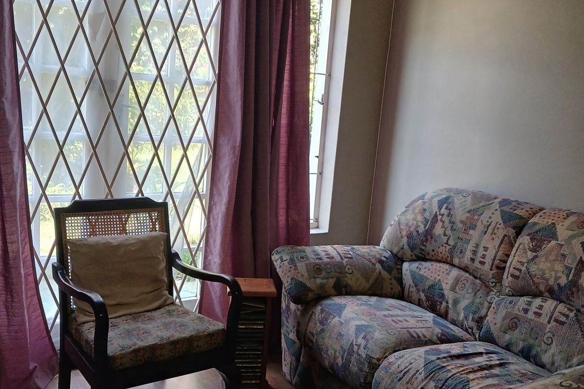A living room area featuring laminate flooring and a large window fitted with a security gate and curtain rod.