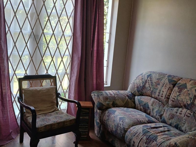 A living room area featuring laminate flooring and a large window fitted with a security gate and curtain rod.
