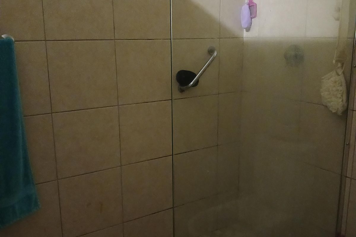 A functional bathroom featuring a glass-enclosed shower with a grab rail and neutral wall tiling.