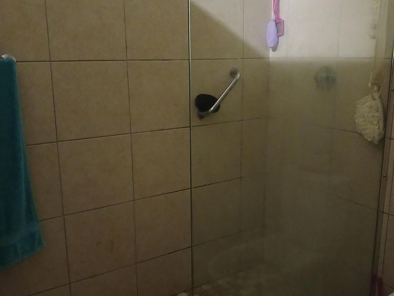 A functional bathroom featuring a glass-enclosed shower with a grab rail and neutral wall tiling.