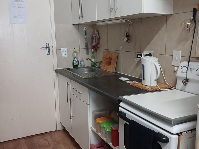 Compact kitchen featuring white cabinetry, laminate countertops, tiled backsplash, and a freestanding stove with wood-look flooring.