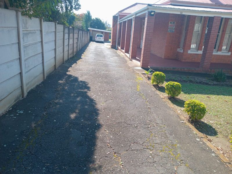 A view of the property's asphalt driveway leading to a garage, featuring a brick facade and a covered veranda.