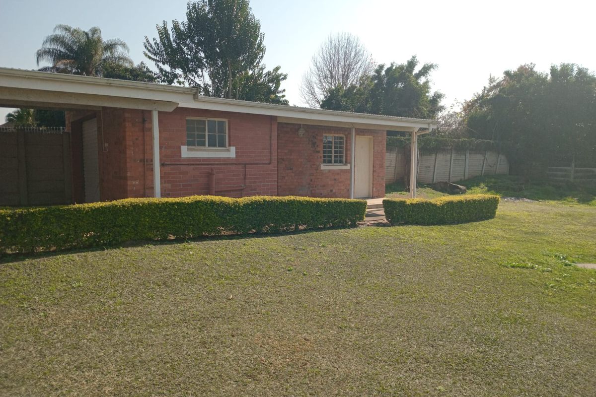 Rear view of a single-story brick house featuring a carport, security-barred windows, and a spacious garden with a precast concrete boundary wall.