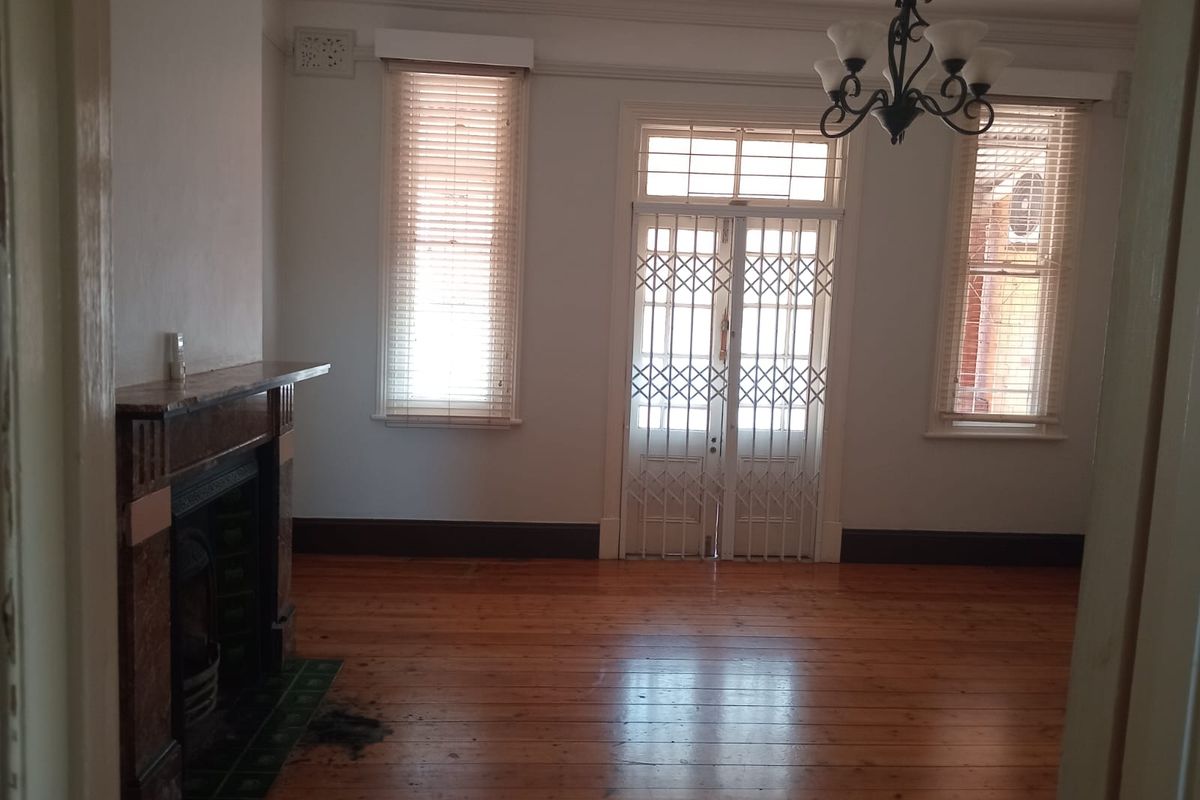 Spacious living room featuring original timber flooring, a classic fireplace, and a secure entrance door with natural light.