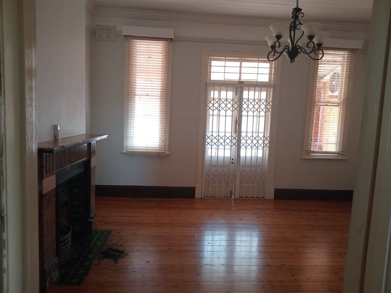 Spacious living room featuring original timber flooring, a classic fireplace, and a secure entrance door with natural light.