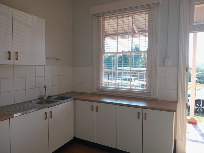 A functional kitchen area featuring white cabinetry, laminate countertops, a stainless steel double sink, and a large sash window providing natural light.