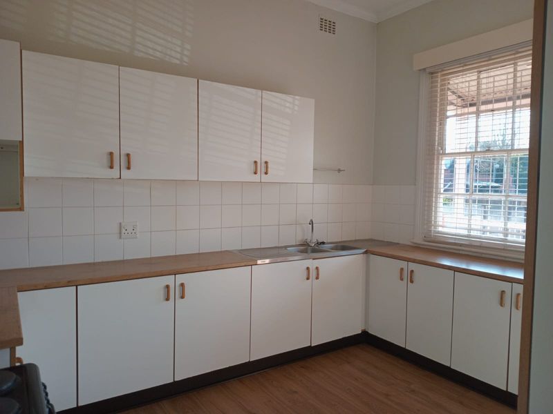 A clean, functional kitchen featuring white cabinetry, laminate countertops, a stainless steel sink, and a large sash window providing natural light.