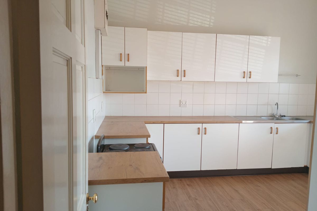 A clean, functional kitchen featuring white cabinetry, wood-look laminate countertops, an electric stove, and a stainless steel sink with a tiled backsplash.