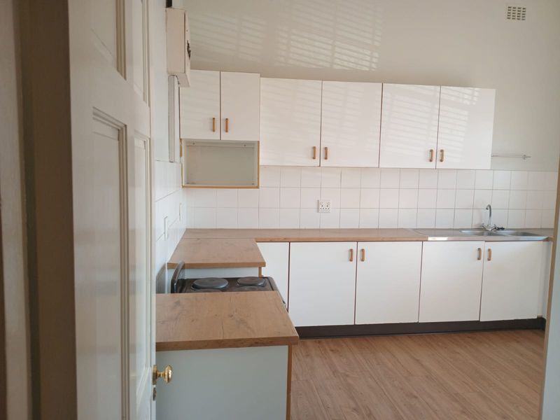 A clean, functional kitchen featuring white cabinetry, wood-look laminate countertops, an electric stove, and a stainless steel sink with a tiled backsplash.