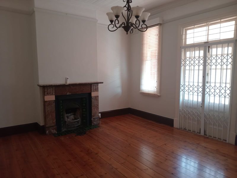 An empty living room featuring original timber flooring, a classic fireplace, and a security gate leading to the exterior.