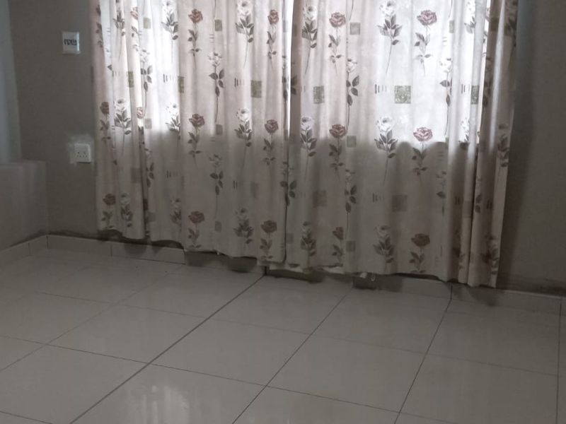 An empty bedroom featuring tiled flooring and neutral walls, showing signs of wear and potential moisture staining near the baseboards.