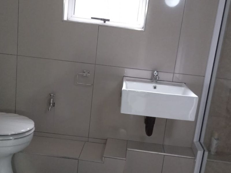 A clean, modern bathroom featuring a wall-mounted basin, toilet, and a glass-enclosed shower with neutral wall tiling.