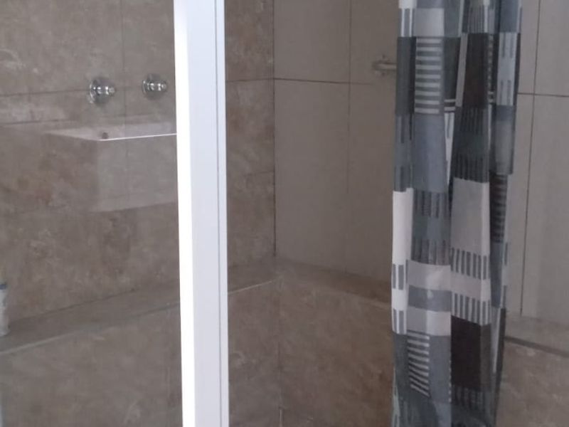 A functional bathroom shower area featuring tiled walls, a glass enclosure, and a shower head with mixer controls.