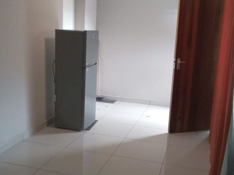 A simple, empty kitchen area featuring neutral tiled flooring and a wooden door, providing a blank canvas for potential layout and design.