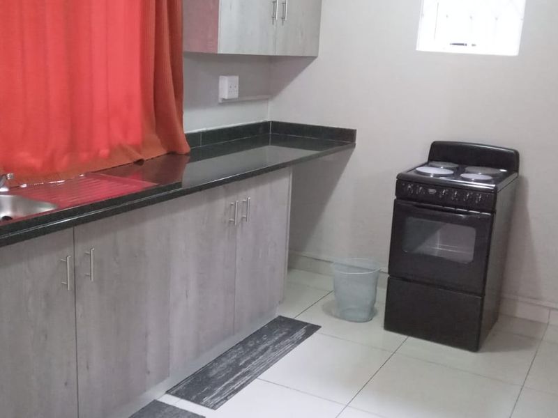A functional kitchen featuring built-in cabinetry, granite countertops, a stainless steel sink, and a freestanding stove with tiled flooring.