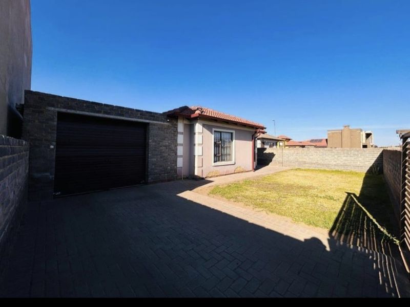 Front view of the property featuring a paved driveway, attached garage, and a private garden area enclosed by boundary walls.