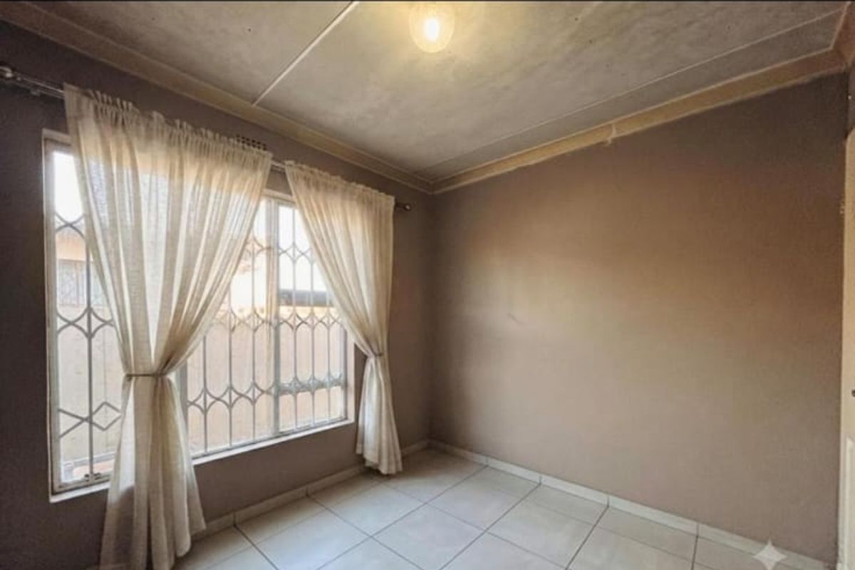 An empty bedroom featuring tiled flooring, a security gate on the window, and neutral wall tones, ready for personalization.