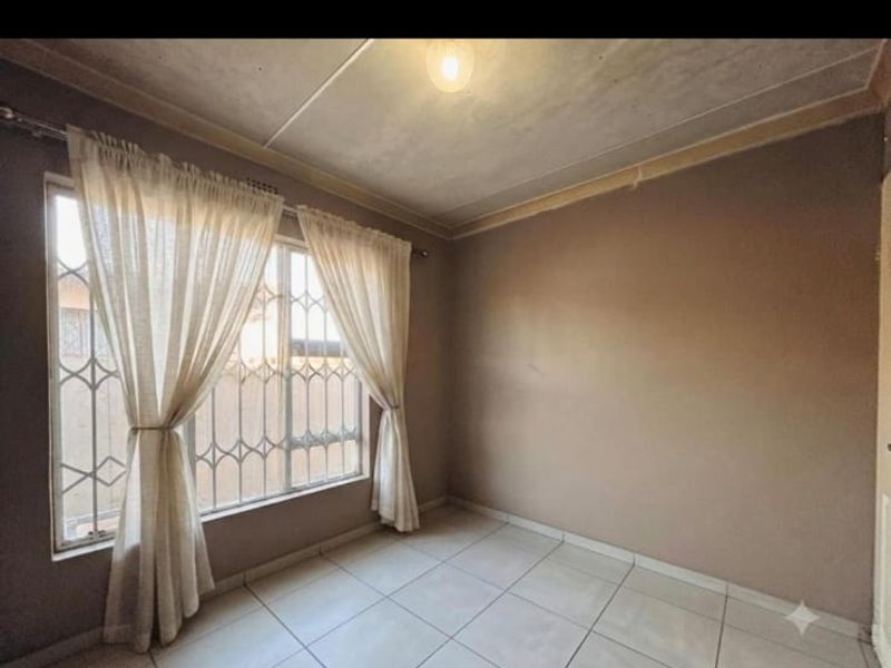 An empty bedroom featuring tiled flooring, a security gate on the window, and neutral wall tones, ready for personalization.