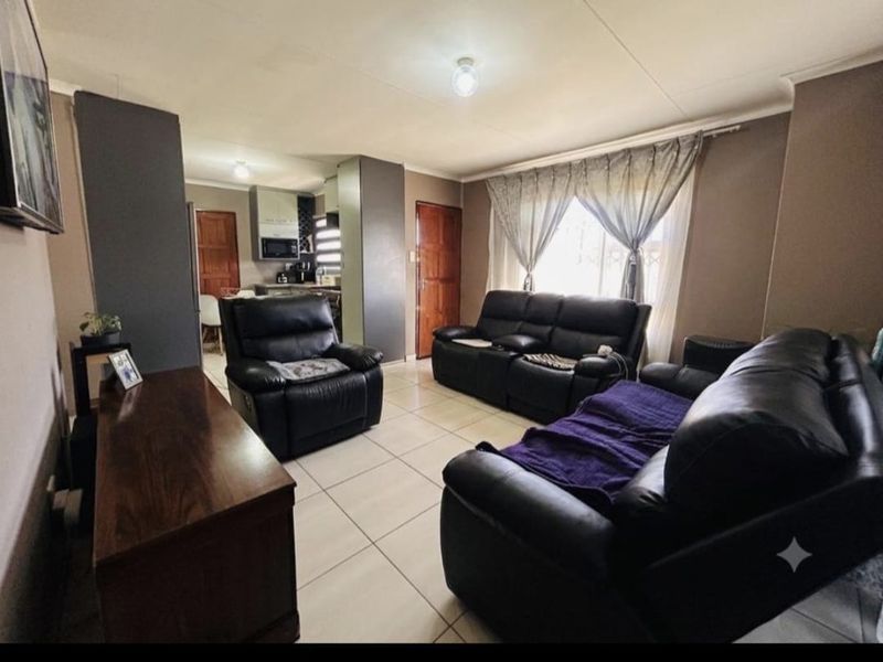 Open plan living area featuring tiled flooring and a connected kitchen space with built-in cabinetry and appliances.