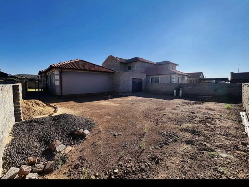 A spacious rear yard area featuring perimeter walling and access to the garage, currently awaiting landscaping and final exterior finishing.