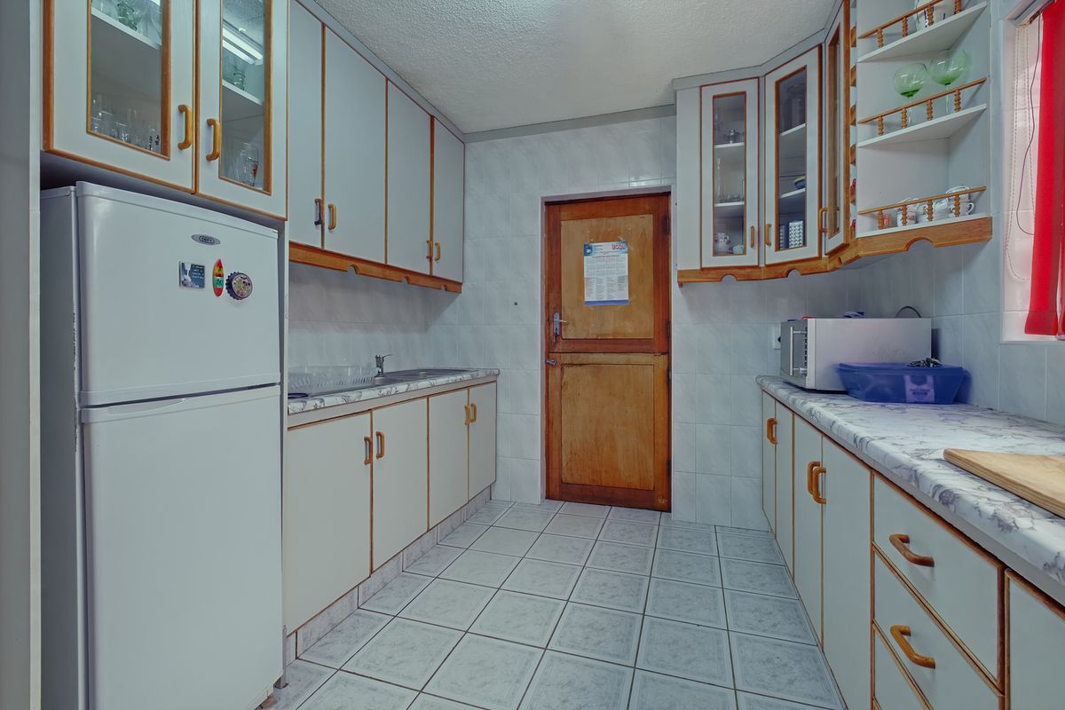 A functional kitchen featuring tiled walls and flooring, ample built-in cabinetry, laminate countertops, and a classic wooden door.