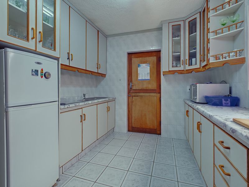 A functional kitchen featuring tiled walls and flooring, ample built-in cabinetry, laminate countertops, and a classic wooden door.