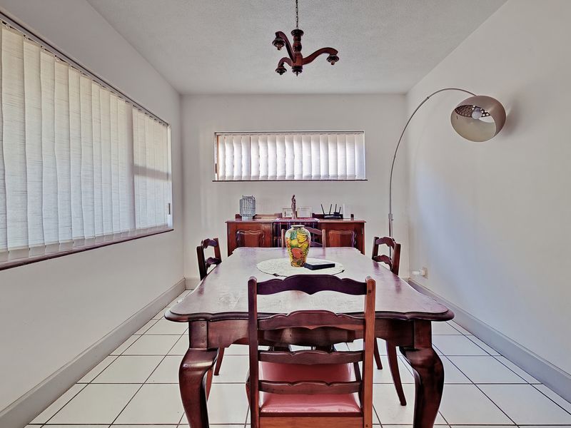 A dining room featuring tiled flooring, vertical blinds on the windows, and a central ceiling light fixture.