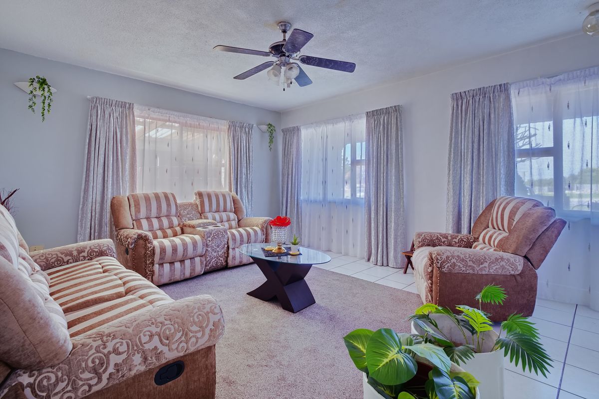 A comfortable living room featuring a ceiling fan, neutral wall tones, and a combination of carpet and tiled flooring with ample natural light.
