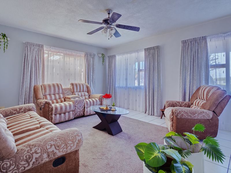A comfortable living room featuring a ceiling fan, neutral wall tones, and a combination of carpet and tiled flooring with ample natural light.