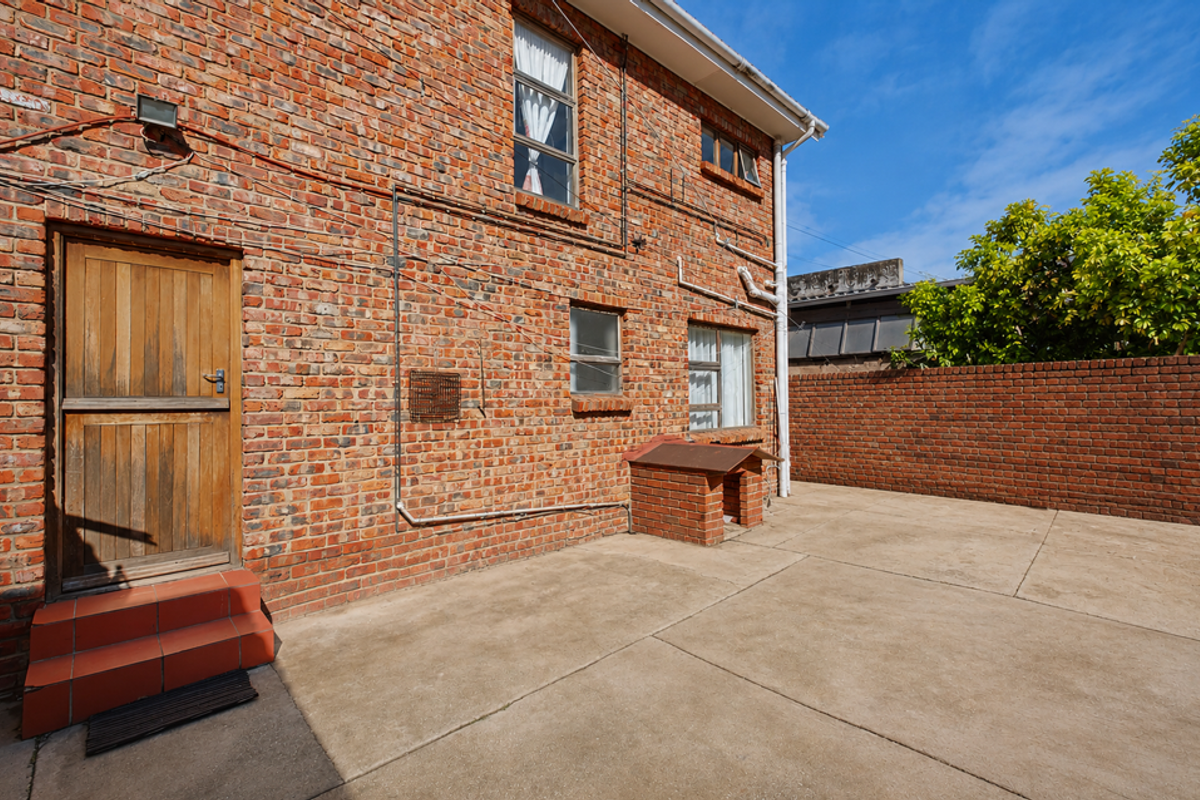 Rear exterior view of the property featuring an exposed brick facade, concrete paved courtyard, and a built-in brick kennel.
