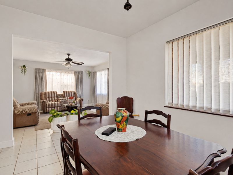 Open plan dining and living area featuring neutral tiled flooring, large windows with vertical blinds, and a ceiling fan.