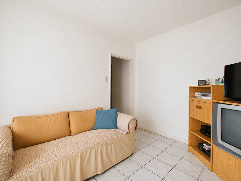 A simple living room area featuring neutral tiled flooring and plain white walls, providing a functional and versatile space.
