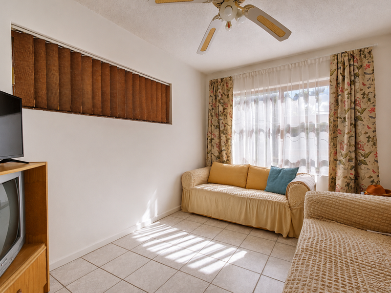 A living room featuring tiled flooring, a ceiling fan, and natural light through a large window with curtains.