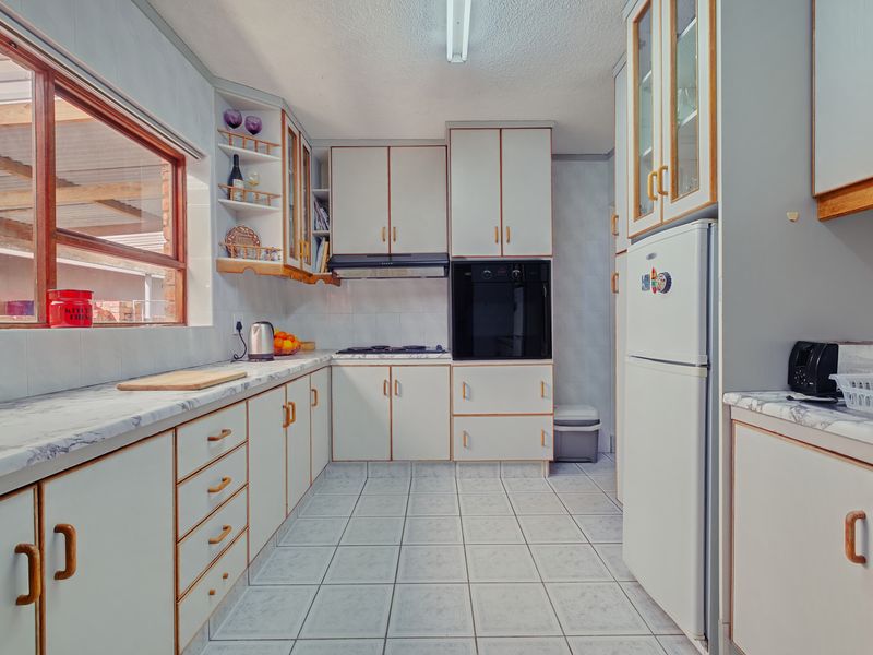 A functional kitchen featuring white cabinetry with wood trim, laminate countertops, built-in oven, hob, and tiled flooring, offering a classic layout with ample storage.
