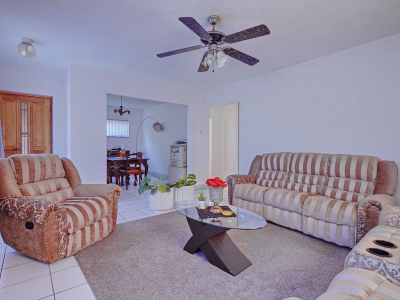 A living room featuring tiled flooring, a ceiling fan, and an open archway leading to an adjacent dining area.