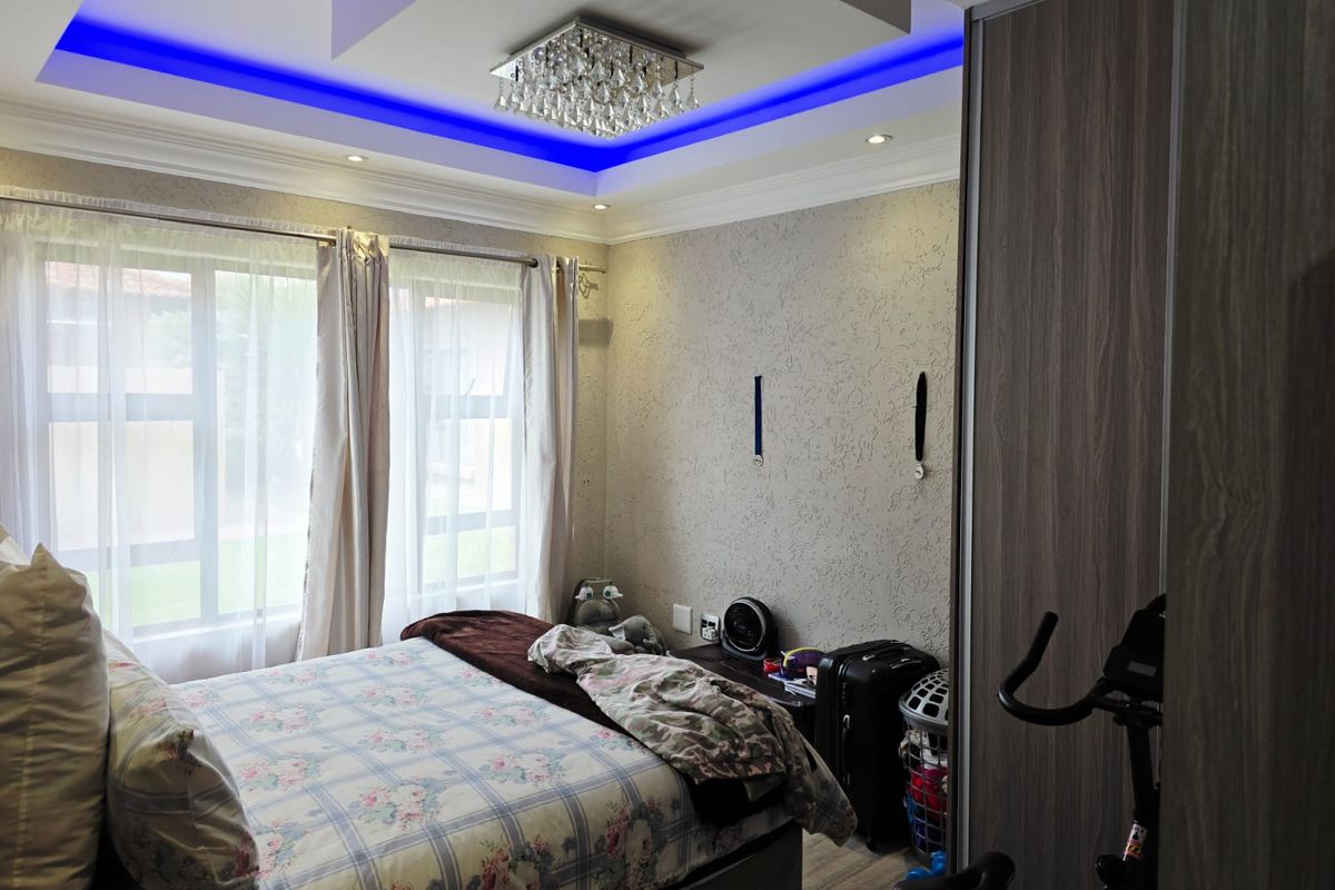 A well-maintained bedroom featuring a decorative tray ceiling with blue accent lighting, recessed downlights, and a built-in wardrobe.