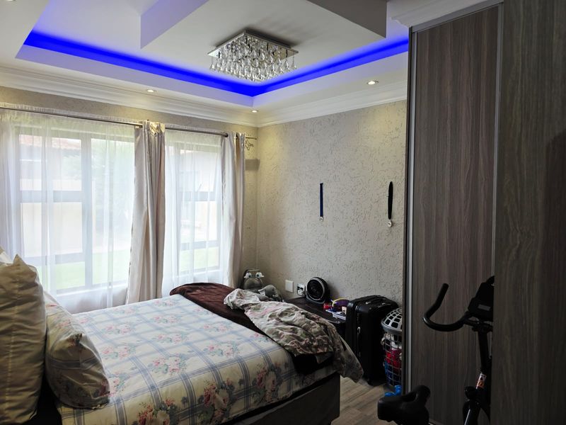 A well-maintained bedroom featuring a decorative tray ceiling with blue accent lighting, recessed downlights, and a built-in wardrobe.