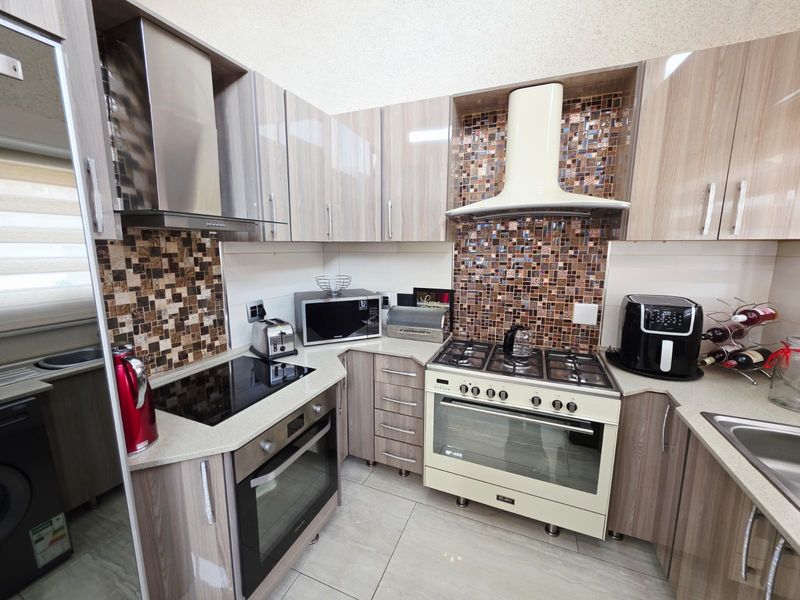 Modern kitchen featuring wood-grain cabinetry, mosaic tile backsplashes, stone countertops, and a dual cooking setup with both electric and gas appliances.