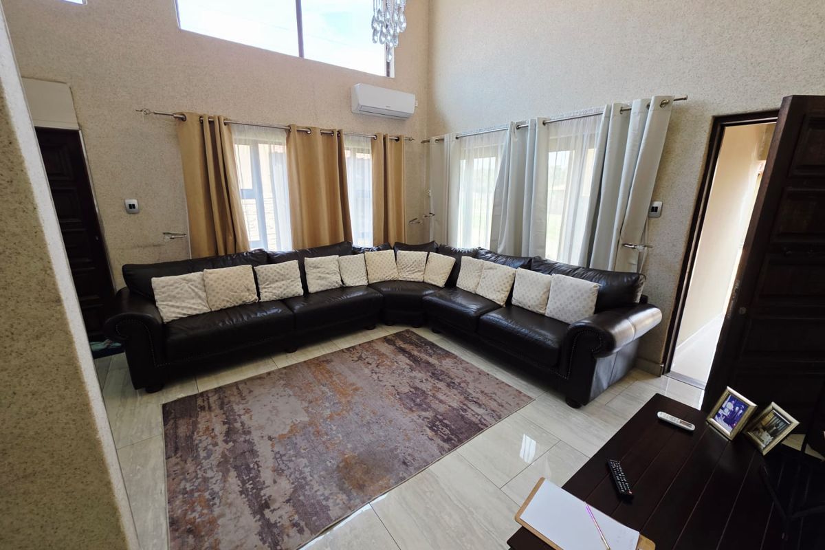 Spacious living room featuring double-volume ceilings, large windows for natural light, polished porcelain floor tiles, and a wall-mounted air conditioning unit.